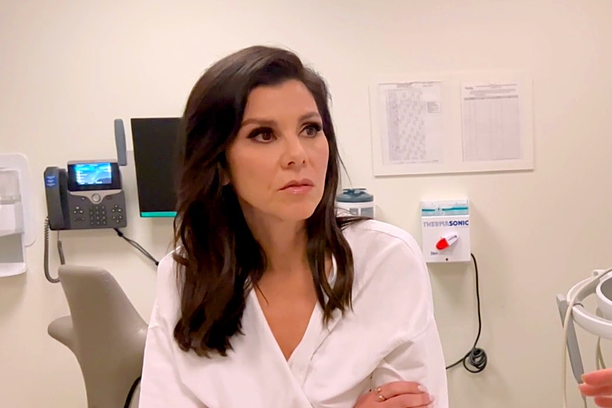 Heather Dubrow sitting in a doctor's office with a white robe on.