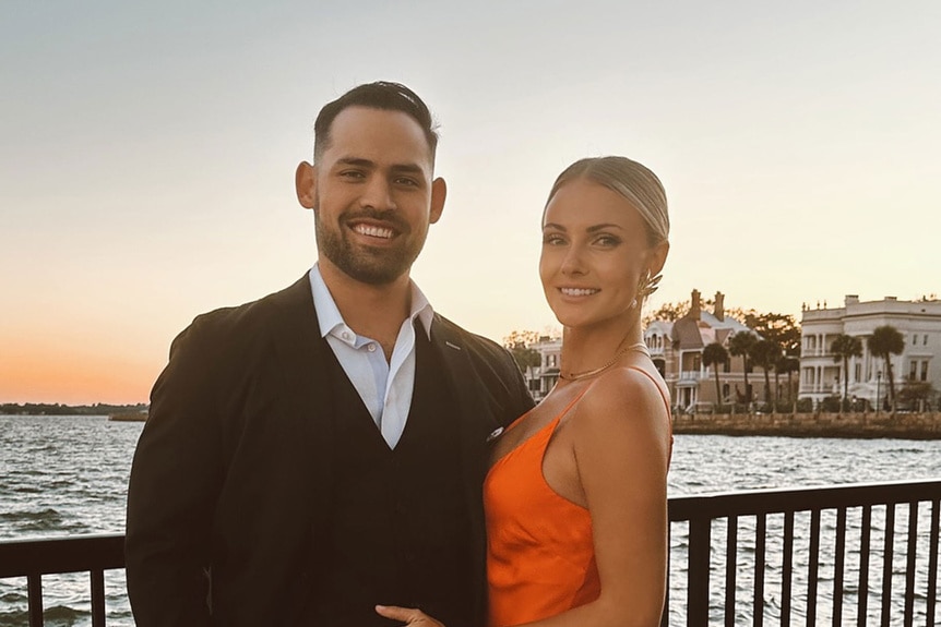 Taylor Ann Green and Gaston Rojas posing together in front of water during sunset.