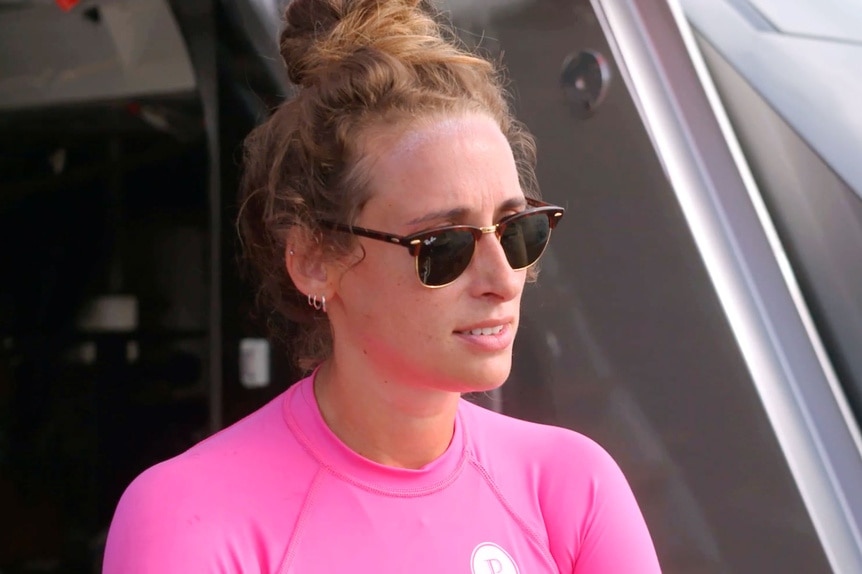 Emma Crouch wearing a pink wet shirt and sunglasses on a yacht deck