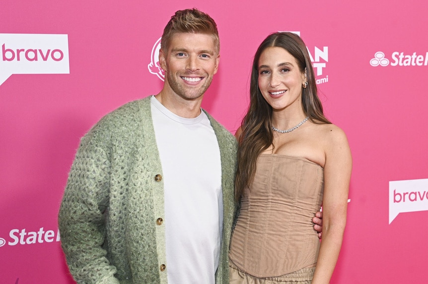 Kyle Cooke and Amanda Batula smile in front of a step and repeat at Bravo Fan Fest 2024.