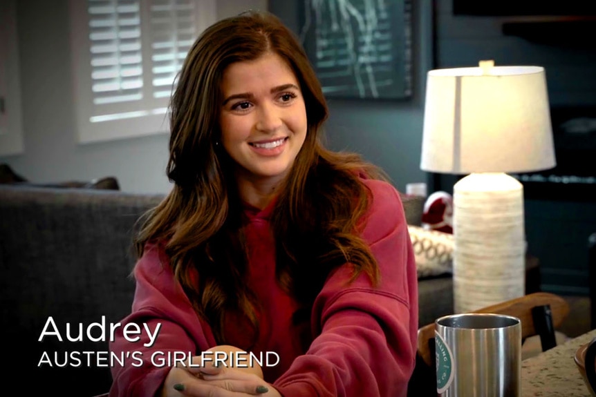 Austen Kroll's Girlfriend Audrey sitting in his living room wearing a red sweatshirt.