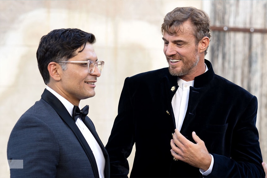 Shep Rose and Rodrigo Reyes wearing tuxedos and having a conversation together.