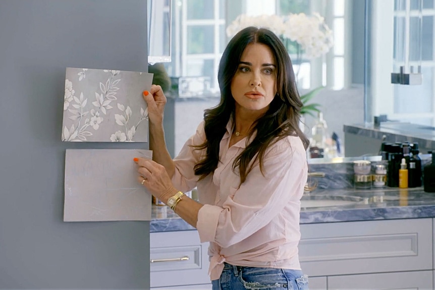 Kyle Richards holding up wallpaper samples for Mauricio Umansky in their home The Real Housewives of Beverly Hills Season 14, Episode 3.