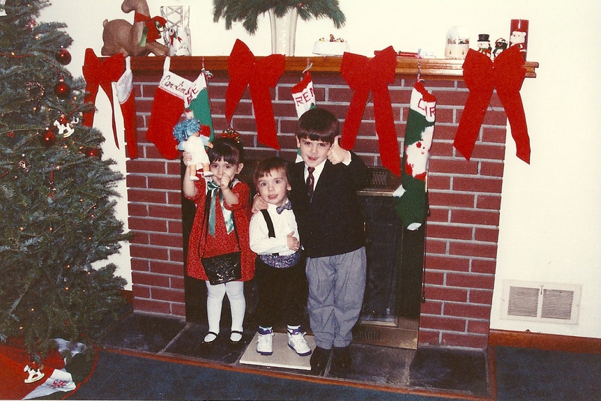 Ashlee Holmes, Nicholas Laurita and CJ Laurita in front of a fireplace decorated for Christmas as children